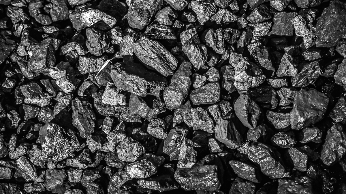 A pile of unprocessed coal briquettes is photographed from above. The image is in shades of gray and black and is more illuminated in the center than along the edges.